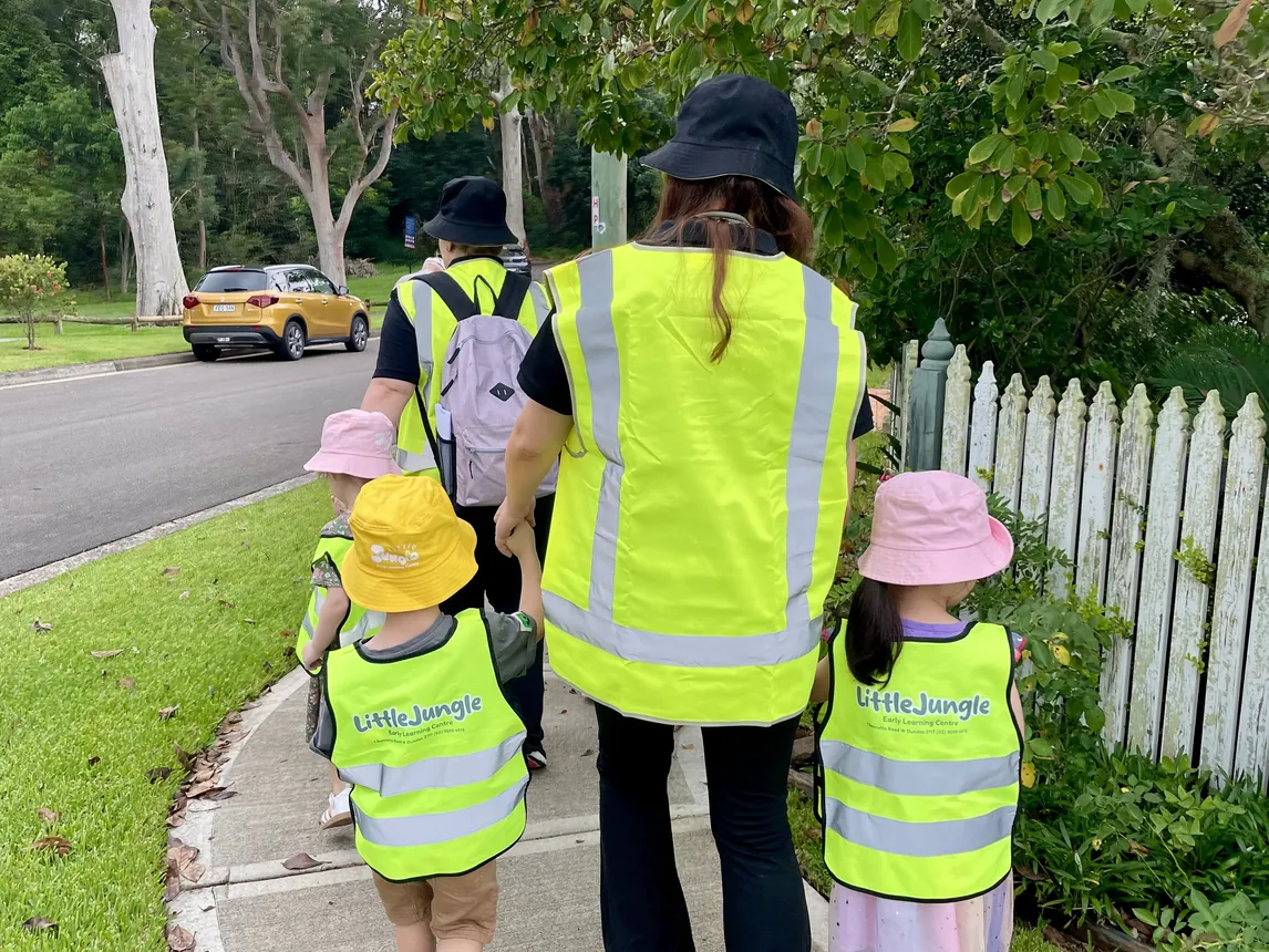 Educator and children in hi-vis vests on a community walk