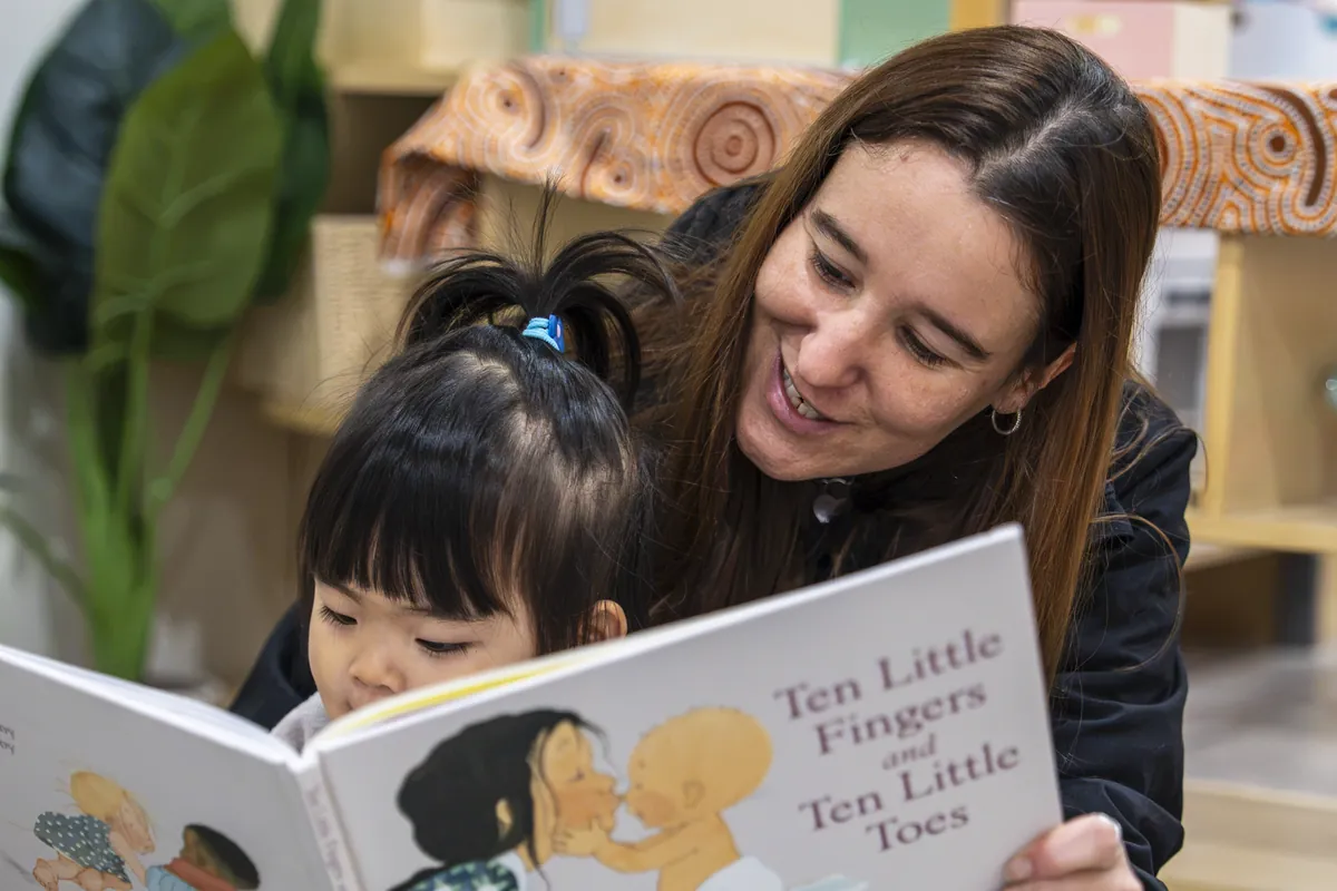 Educator reading Ten Little Fingers and Ten Little Toes with a child on her lap, Little Jungle Dundas