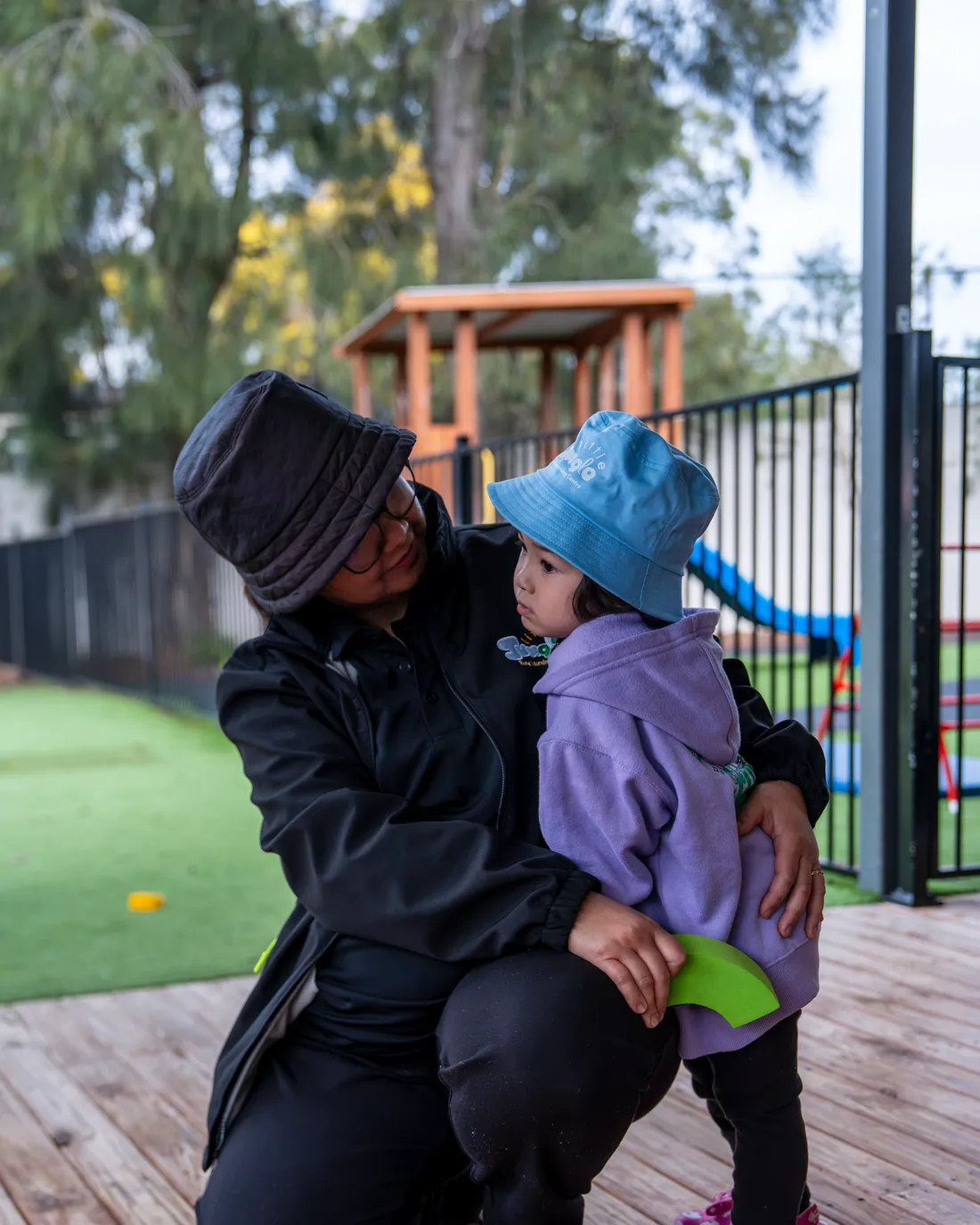 Educator kneeling with an arm around a toddler outdoors, Little Jungle Dundas
