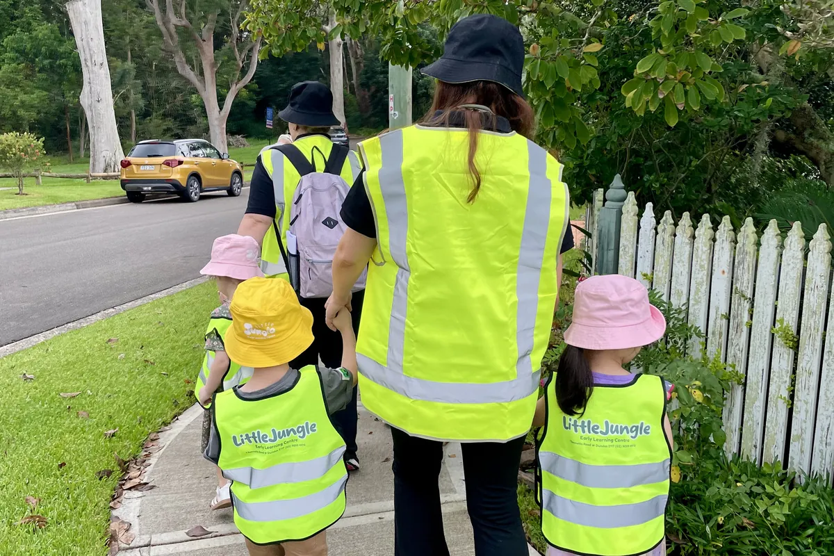 Educator and children in hi-vis vests walking together on a Dundas footpath