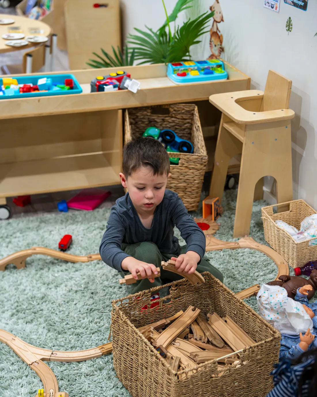 Child building a wooden train track from a basket of pieces, Little Jungle Dundas
