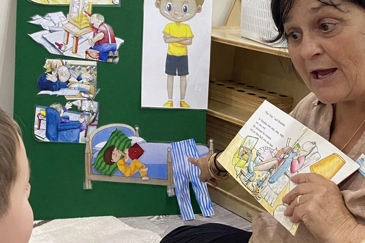 A visitor sharing a picture book and a routine board with a child at Little Jungle Dundas