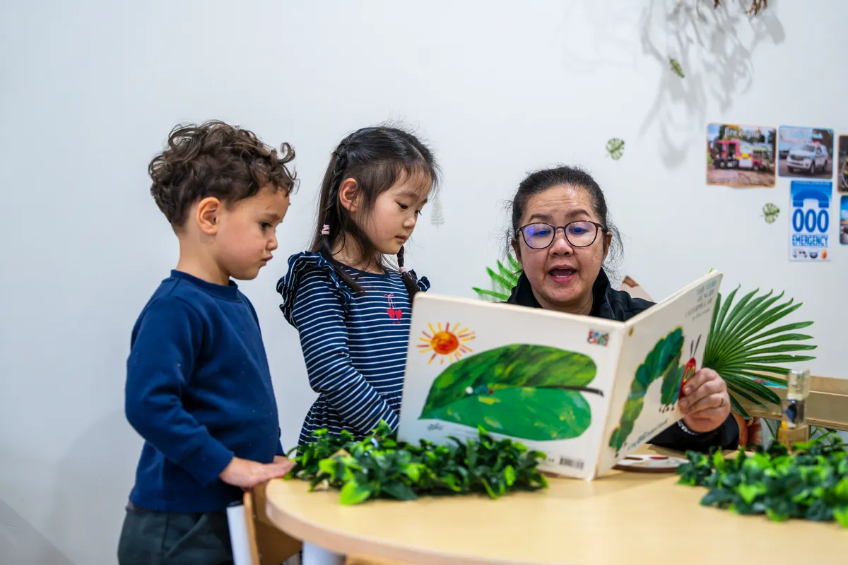 Educator sharing a picture book with two preschoolers at Little Jungle Dundas