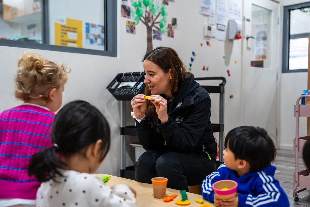 Educator eating at a low table alongside three children at Little Jungle Dundas