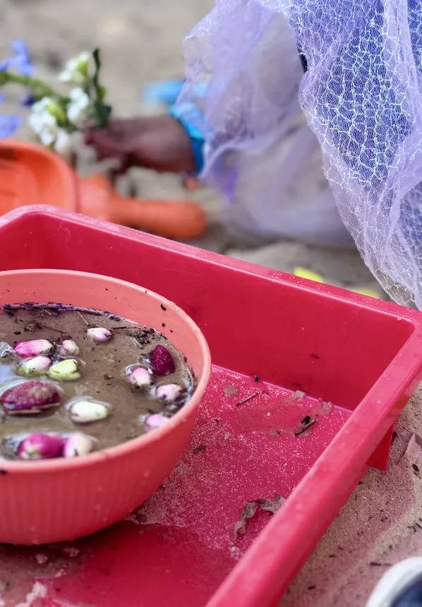 Water and pebbles set out in a sensory tray beside the sandpit