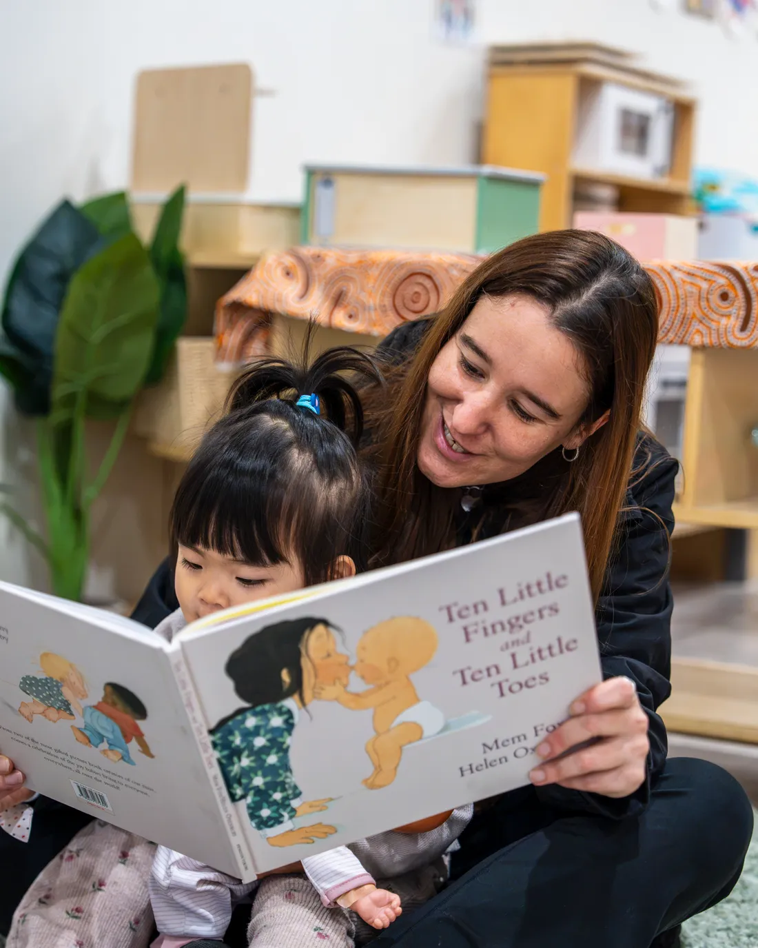Educator reading a picture book to a child on her lap at Little Jungle Dundas